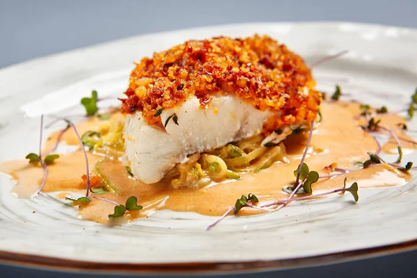 Soslu kızarmış morina filetosu. Restoran yemeği bölümü. Beyaz tabak üzerinde servis edilen hamurlu garnitürlü balık. Ekmek kırıntıları serpiştirilmiş deniz ürünleri. Lüks gurme yemek servisi