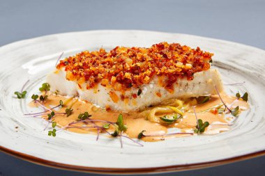 Soslu kızarmış morina filetosu. Restoran yemeği bölümü. Beyaz tabak üzerinde servis edilen hamurlu garnitürlü balık. Ekmek kırıntıları serpiştirilmiş deniz ürünleri. Lüks gurme yemek servisi