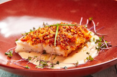 Kırmızı tabakta soslu morina balığı. Domates kırıntılarında pişmiş balık. Kapta deniz ürünleri tabağı var. Lüks restoran yemeği. Yemek pişirme sanatı. Yakından vurucu süslemeli beyaz balık.