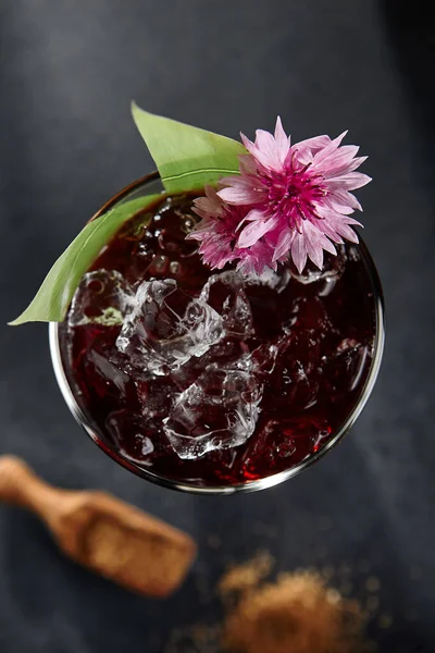 Freshness cocktail with cherry and ice cube. Night party cocktail with pink flower and banana leaf. Tropical drink on dark slate background