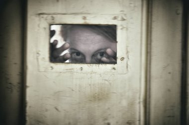 Mentally ill woman looking through a small window i a door at an old mental hospital. Motion blur for efffect. clipart