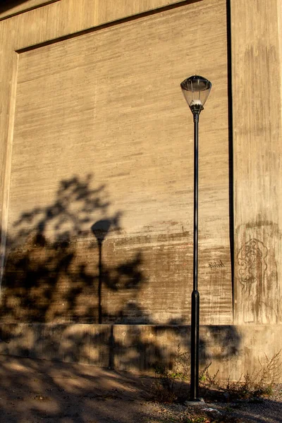 暖かい太陽の光の中で影とコンクリートの壁に対する古いランプポスト ストックフォト