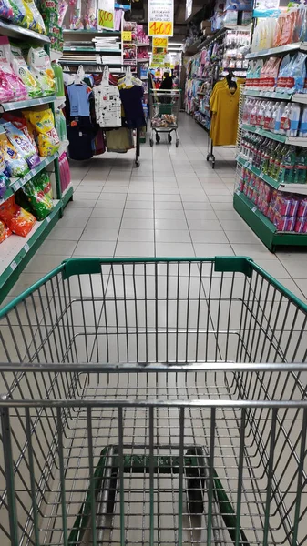 Nákupní košík umístěný mezi regály v supermarketu — Stock fotografie