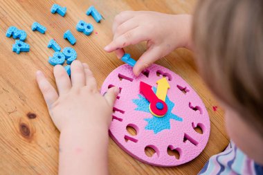 Saat oyuncağıyla zaman geçiren küçük bir çocuk, saati söylemeyi öğrenen bir çocuk, yeni yürümeye başlayan çocuklar için oynayarak öğrenme kavramı..