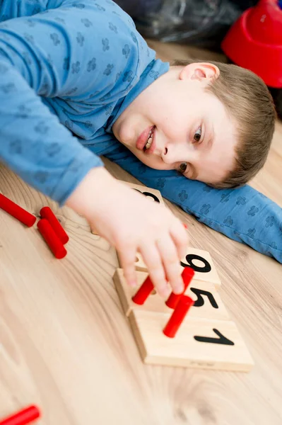 男孩躺在地板上玩计数游戏 插入一根棍子 玩啊学啊数学任务 基本加减额 — 图库照片