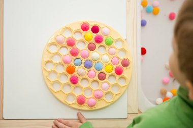 2 yaşında bir çocuk deliğe ponponları sokarak Rus Dumpling Maker 'la oynuyor. Plastik sepette renkli iplik topları