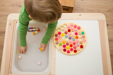 2 yaşında bir çocuk deliğe ponponları sokarak Rus Dumpling Maker 'la oynuyor. Plastik sepette renkli iplik topları