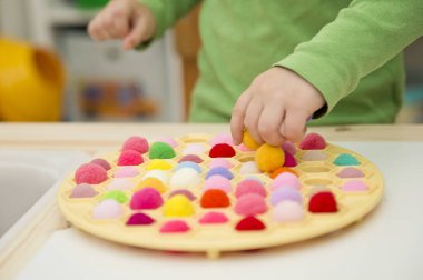 2 yaşında bir çocuk deliğe ponponları sokarak Rus Dumpling Maker 'la oynuyor. Plastik sepette renkli iplik topları