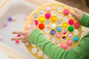 2 yaşında bir çocuk deliğe ponponları sokarak Rus Dumpling Maker 'la oynuyor. Plastik sepette renkli iplik topları