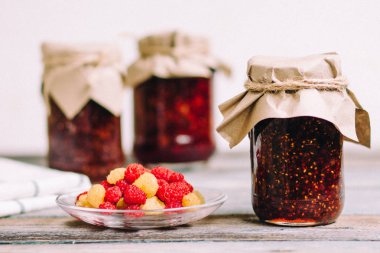 bir tabak ve bardak taze ahududu yemek, ev yapımı tatlılar ahşap bir masa, hazırlıklar, ev yapımı ile ahududu reçeli kavanozlar