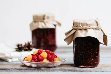 bir tabak ve bardak taze ahududu yemek, ev yapımı tatlılar ahşap bir masa, hazırlıklar, ev yapımı ile ahududu reçeli kavanozlar