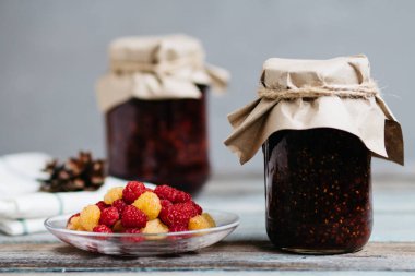 bir tabak ve bardak taze ahududu yemek, ev yapımı tatlılar ahşap bir masa, hazırlıklar, ev yapımı ile ahududu reçeli kavanozlar