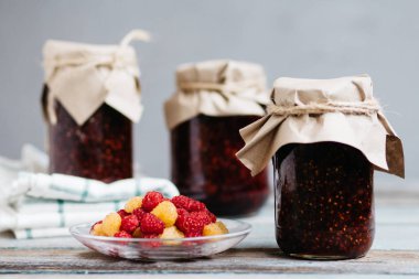 bir tabak ve bardak taze ahududu yemek, ev yapımı tatlılar ahşap bir masa, hazırlıklar, ev yapımı ile ahududu reçeli kavanozlar