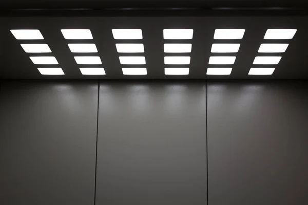 Gray metal elevator with square lamps in the ceiling