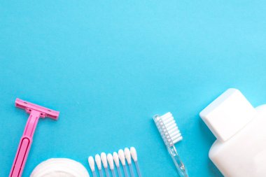 üstten görünüm kişisel bakım ürünleri. Beyaz şişe, pembe ustura, kulak sopa, Pamuklu ped, mavi zemin üzerine diş fırçası. kopya alanı