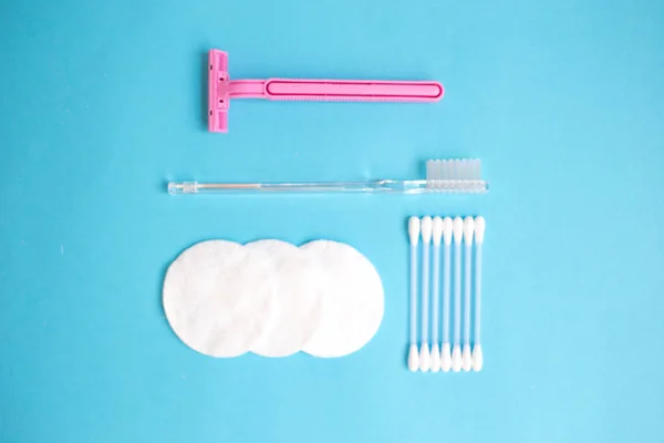 top view personal care products. white bottle, pink razor, ear sticks, cotton pads, toothbrush on blue background. copy space