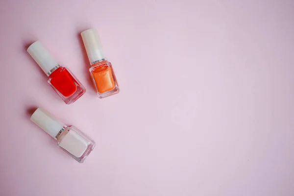 multi-colored nail polishes on pastel pink background, top view, Flat lay. Many round jars with multi-colored for nail polish.