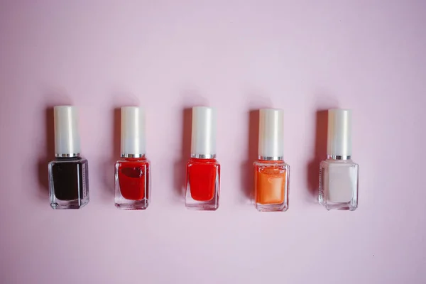 multi-colored nail polishes on pastel pink background, top view, Flat lay. Many round jars with multi-colored for nail polish.
