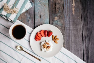 Odaya Servis Kahvaltı süzme peynir, çilek ve fındık ile bir tabak, bir fincan kahve ve bir ahşap masa, sağlıklı gıda, havlu