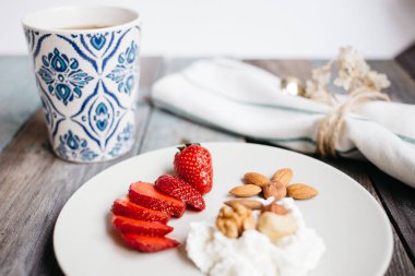 Odaya Servis Kahvaltı süzme peynir, çilek ve fındık ile bir tabak, bir fincan kahve ve bir ahşap masa, sağlıklı gıda, havlu