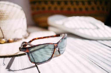 Bir şapka, beyaz flip flop, güneş gözlüğü, plaj çantası beyaz ahşap arka planda, sert ışık