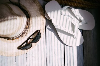 Bir şapka, beyaz flip flop, güneş gözlüğü, plaj çantası beyaz ahşap arka planda, sert ışık