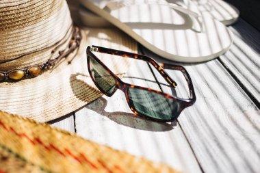 Bir şapka, beyaz flip flop, güneş gözlüğü, plaj çantası beyaz ahşap arka planda, sert ışık