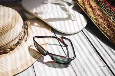 Bir şapka, beyaz flip flop, güneş gözlüğü, plaj çantası beyaz ahşap arka planda, sert ışık