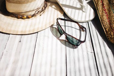 Bir şapka, beyaz flip flop, güneş gözlüğü, plaj çantası beyaz ahşap arka planda, sert ışık