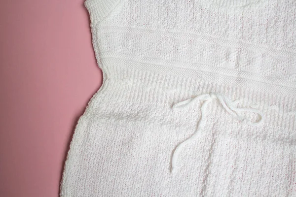 Pembe bir arka plan üzerinde beyaz bebek örgü elbise.