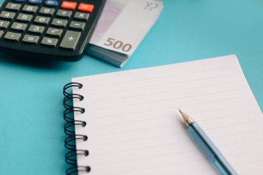 Defter, kalem, Euro banknot sürüsü ve mavi bir arka plan üzerinde bir hesap makinesi