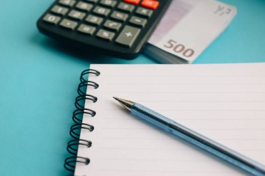 Defter, kalem, Euro banknot sürüsü ve mavi bir arka plan üzerinde bir hesap makinesi