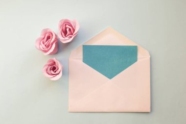 üstten görünüm beyaz zarf, üç gül çiçek, mavi mavi bir arka plan boş karta pembe. En az düz yatıyordu