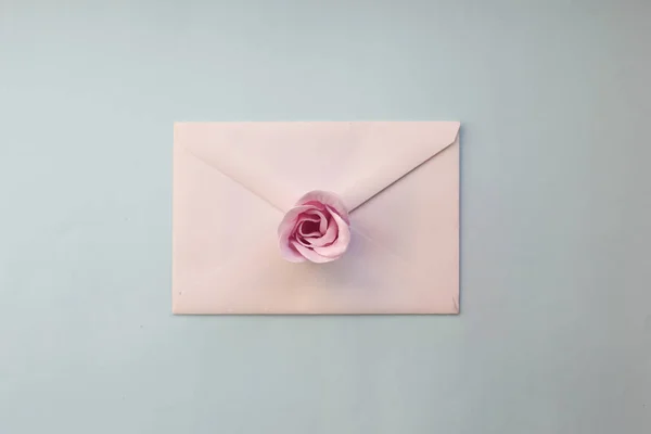 a white envelope, pink rose flower on a blue background. Minimal Flat lay