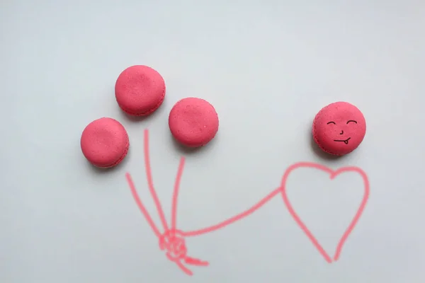 Mavi bir arka plan üzerinde bir adam elinde balon şeklinde üç pembe macaroons.