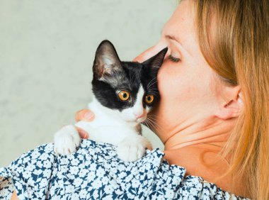Sevimli bir kediyi kucaklayan, okşayan ve öpen sıradan giyinmiş bir kadının hayat tarzı fotoğrafı. Kedi, kızların kollarında olmaktan hoşlanıyor. Seçici odak.