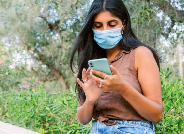 Kapanış sırasında dışarıda mola veren bir kadın, dijital tabletini okurken, CVid-19 'a karşı koruyucu bir maske takıyor.