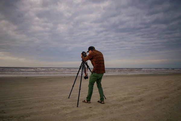 Beach fotograaf met behulp van een statief onder bewolkte hemel — Stockfoto