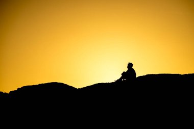 Gün batımında Tofino, British Columbia yakınlarındaki büyük bir kayanın üzerinde oturan insanların silueti..