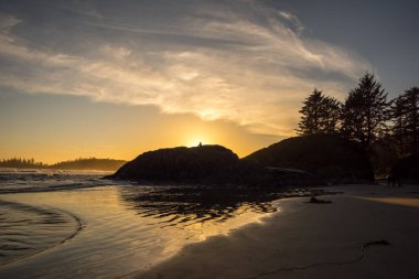Büyük bir kaya çıkıntısının silueti ve Kanada 'nın Vancouver Adası' ndaki Pasifik Kıyısı Ulusal Park Rezervi 'nde günbatımının yansıması.
