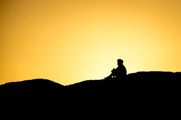 夕日にブリティッシュコロンビア州トフィーノ近くの大きな岩の上に座っている人々のシルエット ロイヤリティフリーのストック画像