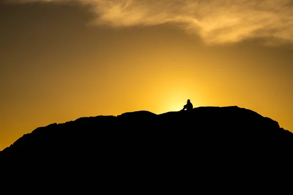夕日にブリティッシュコロンビア州トフィーノ近くの大きな岩の上に座っている人々のシルエット ストック画像