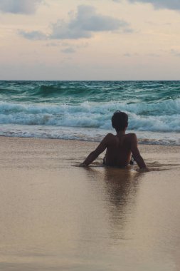 Çocuk suda oturan ve güneş batışını okyanus dalgaları izlerken