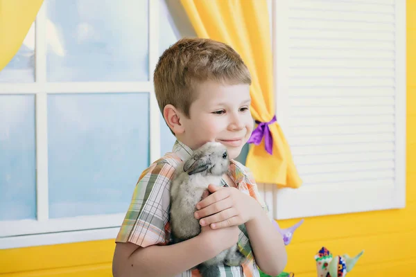 男の子は 彼の手でウサギを保持は 笑みを浮かべてします 明るい黄色の部屋の中の少年 — ストック写真