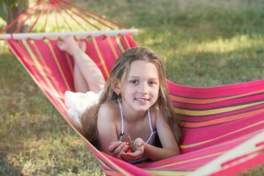 Kırmızı bir hamak beyaz elbiseli bir kız yatıyor. Kız çilek, hastası kiraz. Bir kız bir kiraz ile onun elinde gülümsüyor.