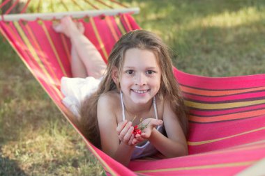 Kırmızı bir hamak beyaz elbiseli bir kız yatıyor. Kız çilek, hastası kiraz. Bir kız bir kiraz ile onun elinde gülümsüyor.