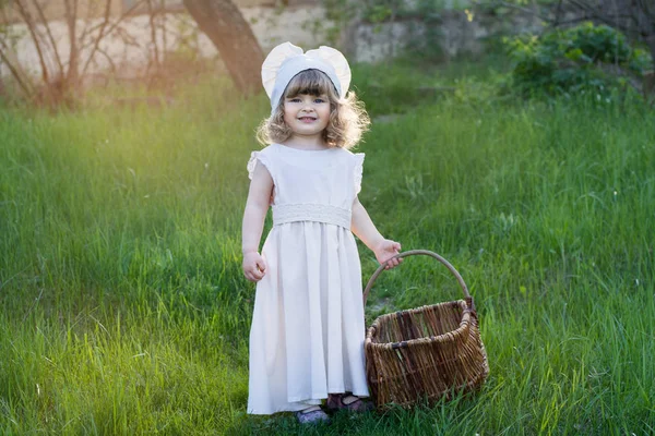 田舎の美しい少女が歩いています 白いドレスの彼女の手の籐のバスケットとの子 夕日の写真 — ストック写真