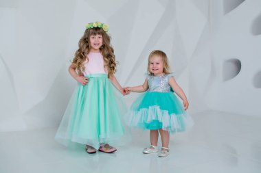 Beyaz bir odada elbise giymiş güzel çocuklar. Kızlar oynar ve güler.