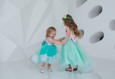 Beyaz bir odada elbise giymiş güzel çocuklar. Kızlar oynar ve güler.