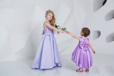 Beyaz bir odada elbise giymiş güzel çocuklar. Kızlar oynar ve güler.